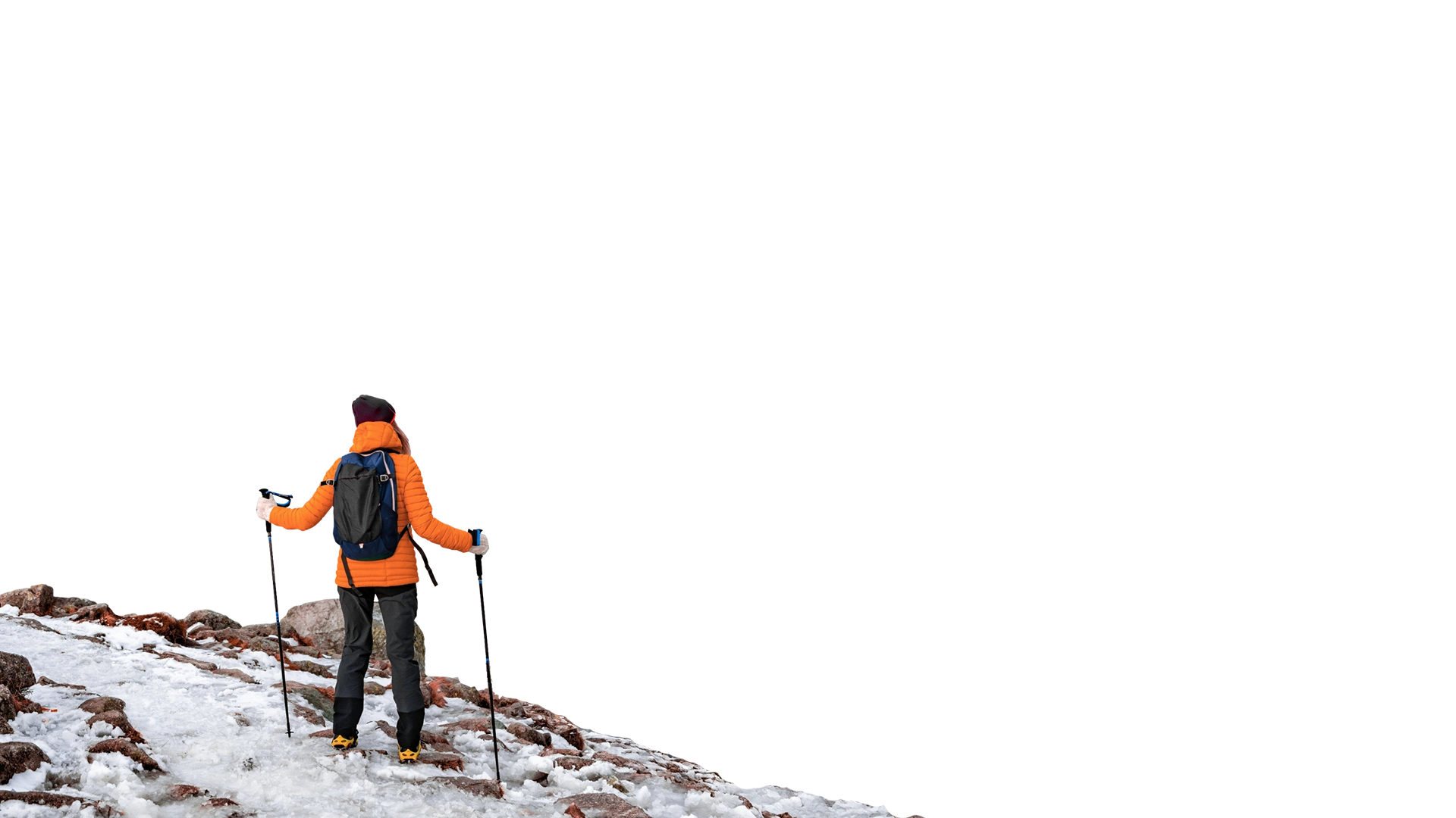 Eine Person mit Rucksack, Winterkleidung und Wanderstöcken. Die Person steht an einer Anhöhe